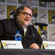 Guillermo del Toro sits at a San Diego Comic-Con dais and speaks into a microphone.
